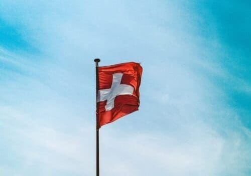 A low angle shot of Switzerland flag on a pole under the breathtaking cloudy sky