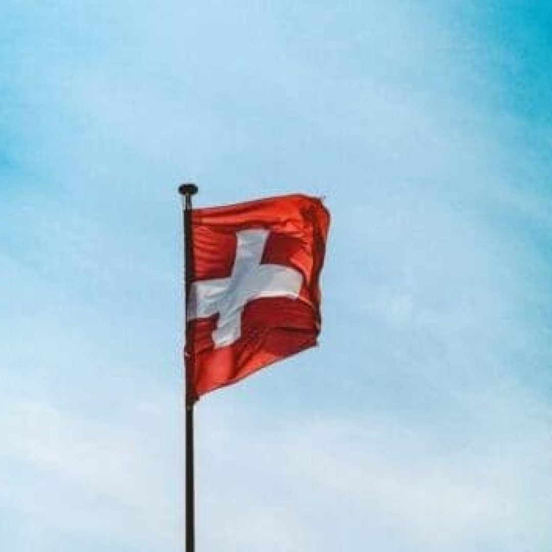 A low angle shot of Switzerland flag on a pole under the breathtaking cloudy sky